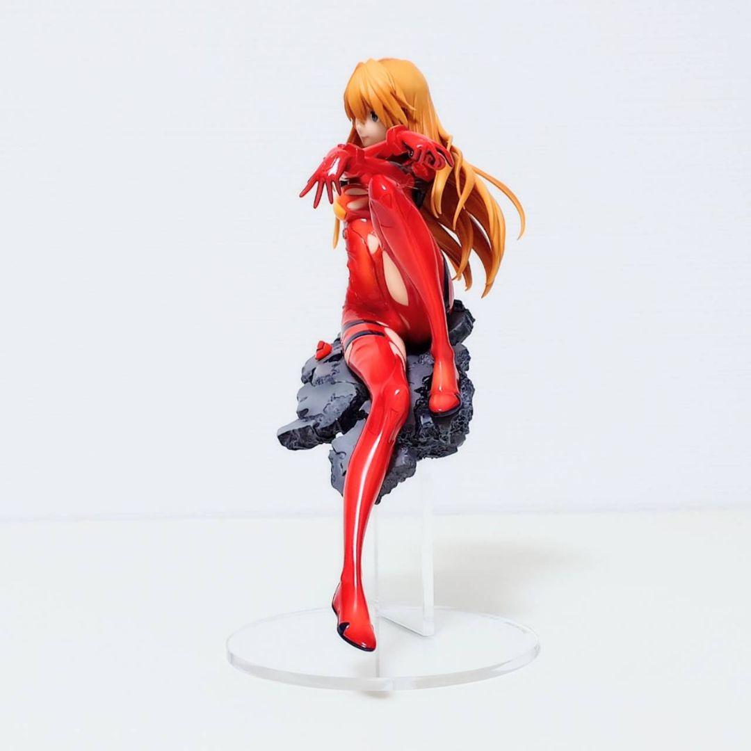 Angled view of Asuka Langley Soryu figure in red plugsuit with long orange hair, seated smiling on a grey rubble base