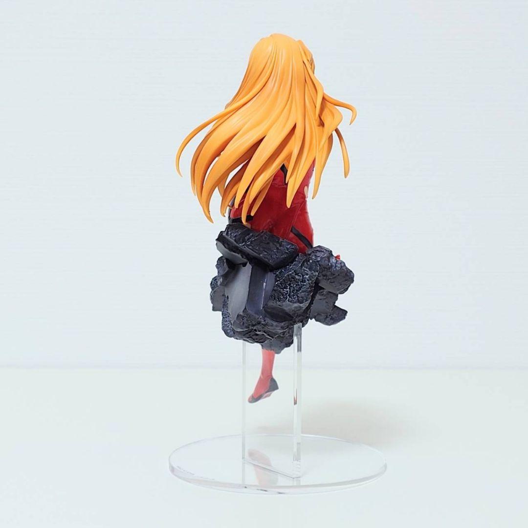 Back of Asuka Langley Soryu figure in red plugsuit with long orange hair, seated smiling on a grey rubble base 