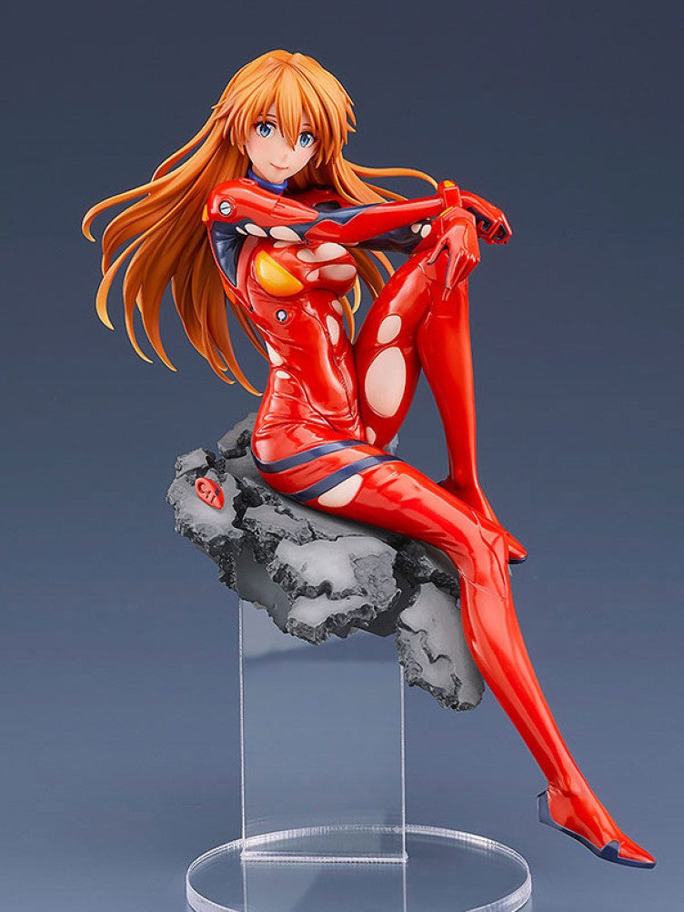 Asuka Langley Soryu figure in red plugsuit with long orange hair, seated smiling on a grey rubble base