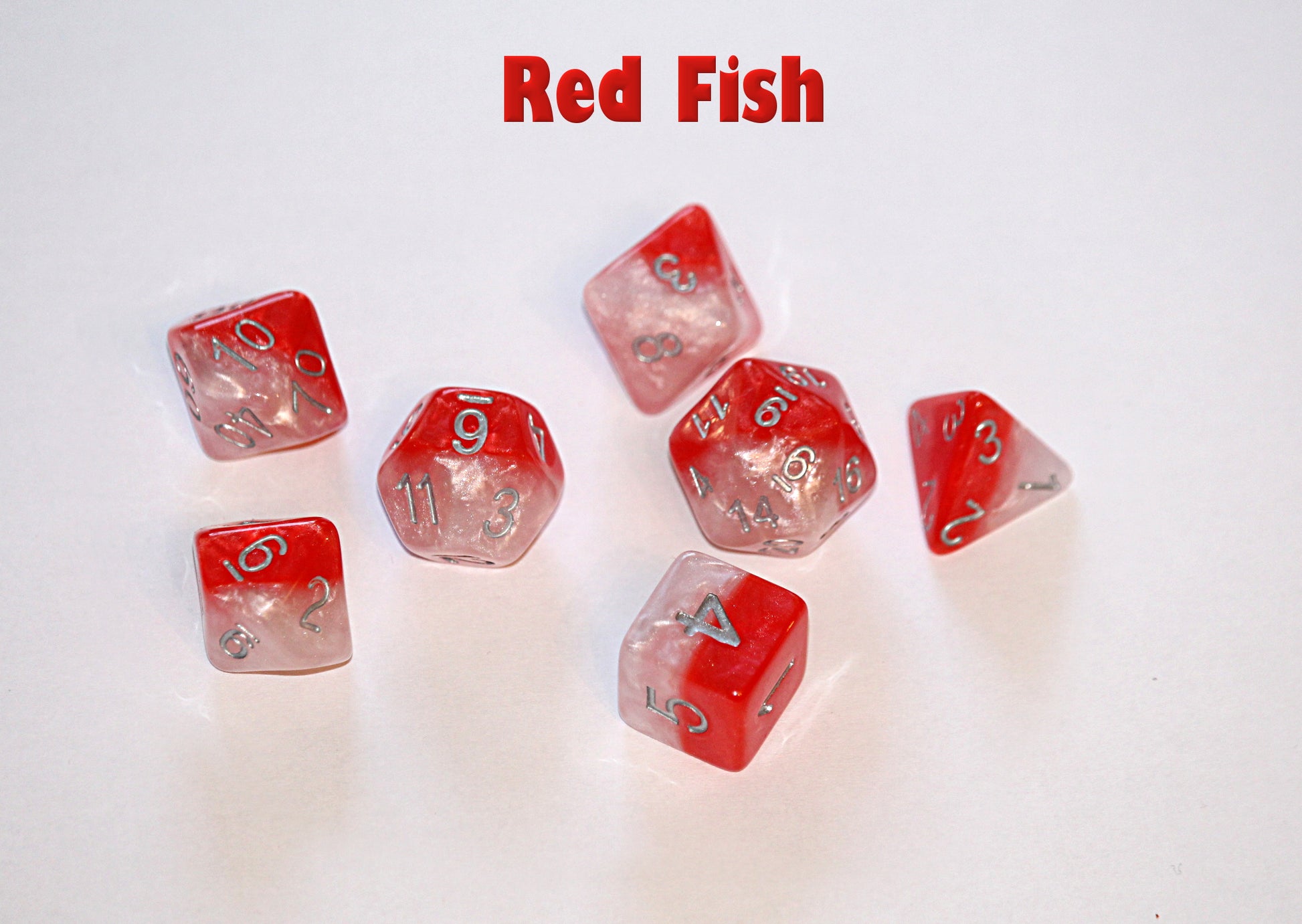 Text "Red Fish" above seven red and white swirled polyhedral dice with silver numbers, scattered on a white surface.
