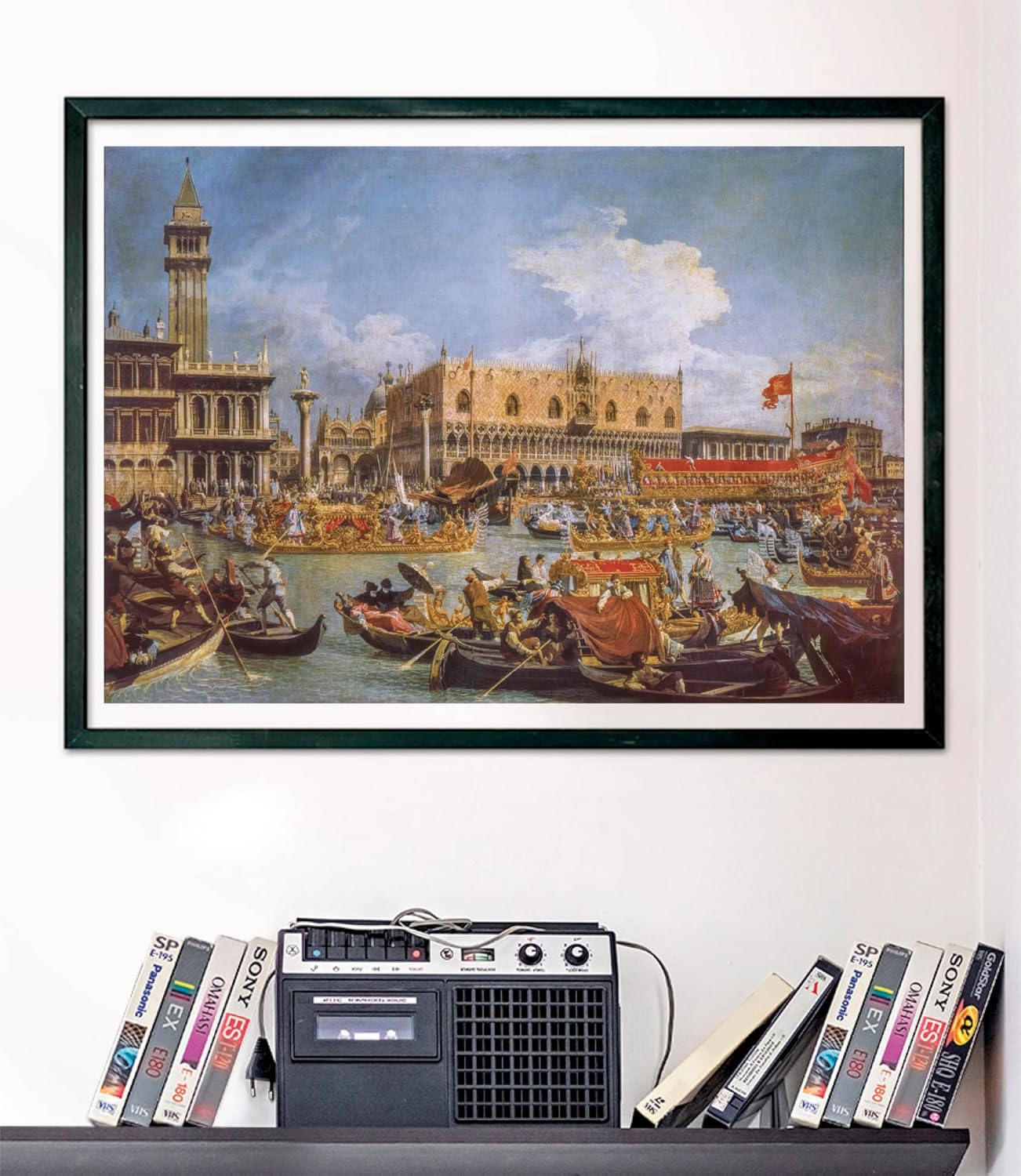 A framed painting of a bustling Venetian canal with many boats and grand buildings, above a retro cassette player and VHS tapes