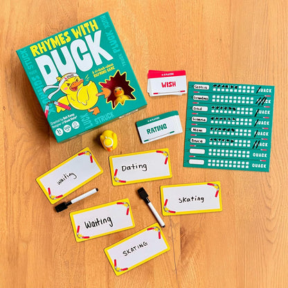 Rhymes with Duck rhyming board game on a wooden table, showing its box, word cards, score sheet, player cards, dry-erase markers, and a yellow rubber duck