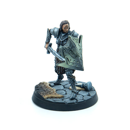Miniature fantasy warrior in dark armor with face markings, holding a sword and ornate shield, on a cobblestone base with fur
