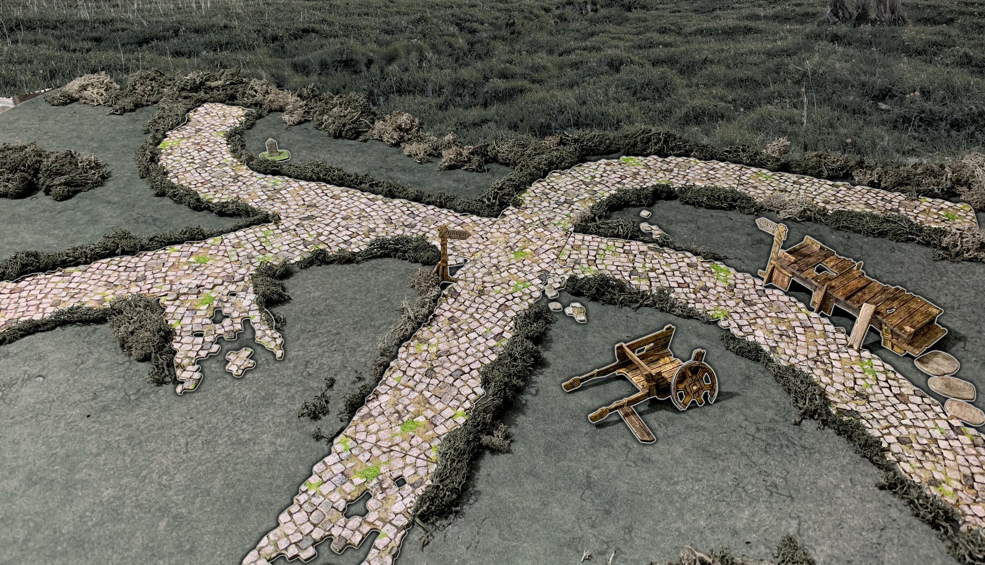 A tabletop game terrain depicting a cobblestone crossroads with a "Haven" sign, broken cart, bridge, and tombstone.