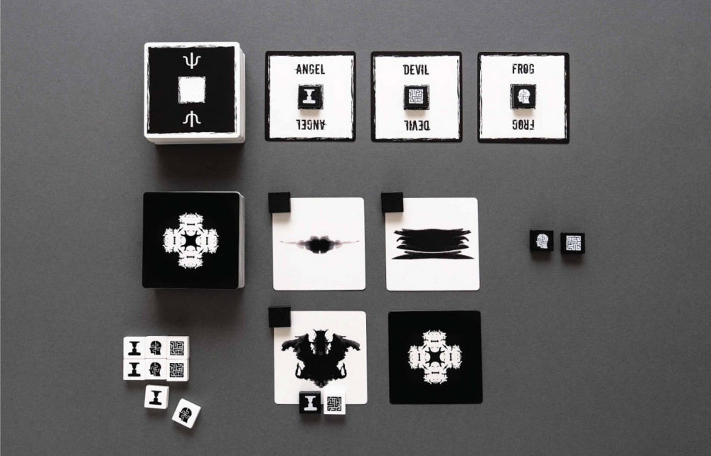 Overhead view of a Rorschach-inspired black and white abstract card and dice game on a dark gray background