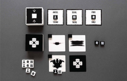 Overhead view of a Rorschach-inspired black and white abstract card and dice game on a dark gray background