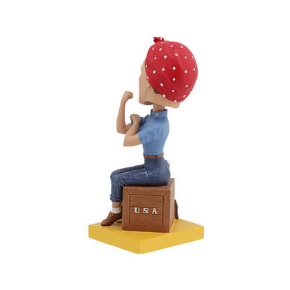 Rosie the Riveter bobblehead with red polka dot bandana flexing arm while seated on a brown crate labeled USA