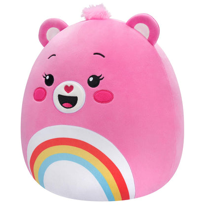 A 10 inch pink Squishmallow Care Bear plush with small ears, a fuzzy pink top knot, and a smiling embroidered face above a vibrant rainbow belly design