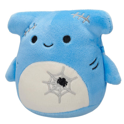 A blue Squishmallow plush toy with a smiling face, grey stitches on its head, and a white belly featuring an embroidered spiderweb and black spider