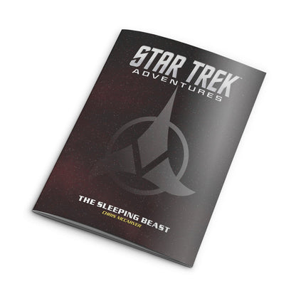 A softcover Star Trek Adventures RPG book, 'The Sleeping Beast,' with a starry cover and Starfleet insignia