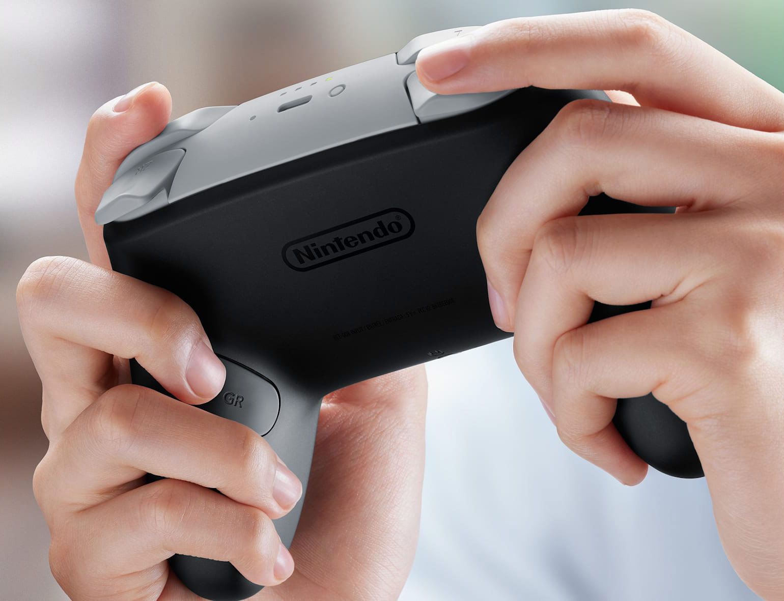 Hands hold a black and grey Nintendo Switch 2 Pro Controller, showing the Nintendo logo