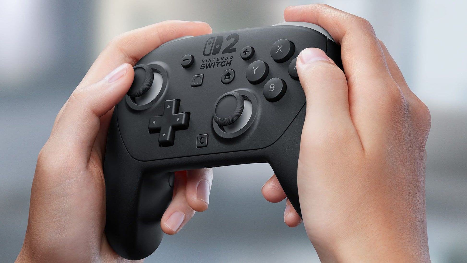 Hands hold a black video game controller featuring a "Nintendo Switch 2" logo and classic button layout