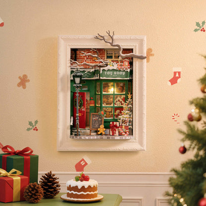 Framed miniature diorama of a green Christmas Toy Shop facade, with gifts and pinecones below