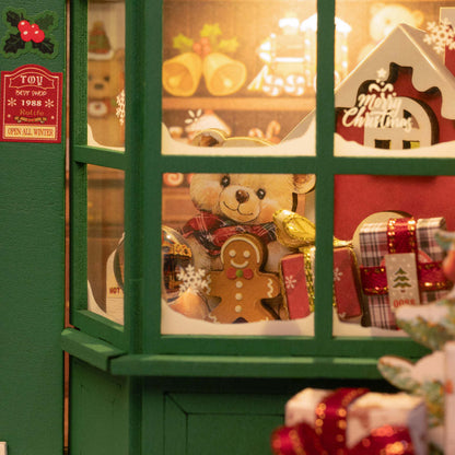 A miniature Christmas toy shop window display featuring a teddy bear and gingerbread man in the snow