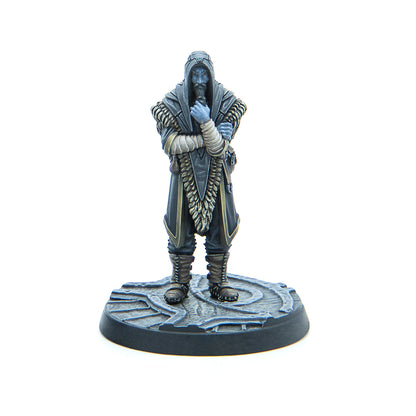 A blue-skinned, bearded miniature figure in a dark hooded robe stands with arms crossed, hand to chin, on a textured circular base