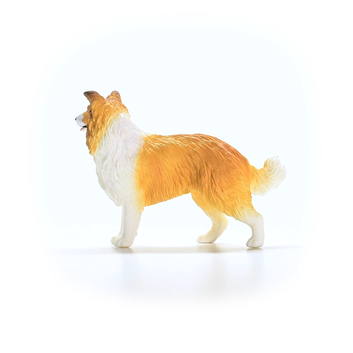 Side view of a tan and white Collie dog figurine standing on a white background