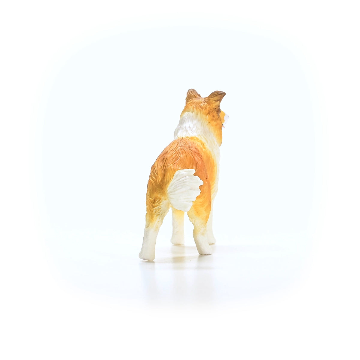 Orange and white dog figurine, seen from the rear, looking over its right shoulder