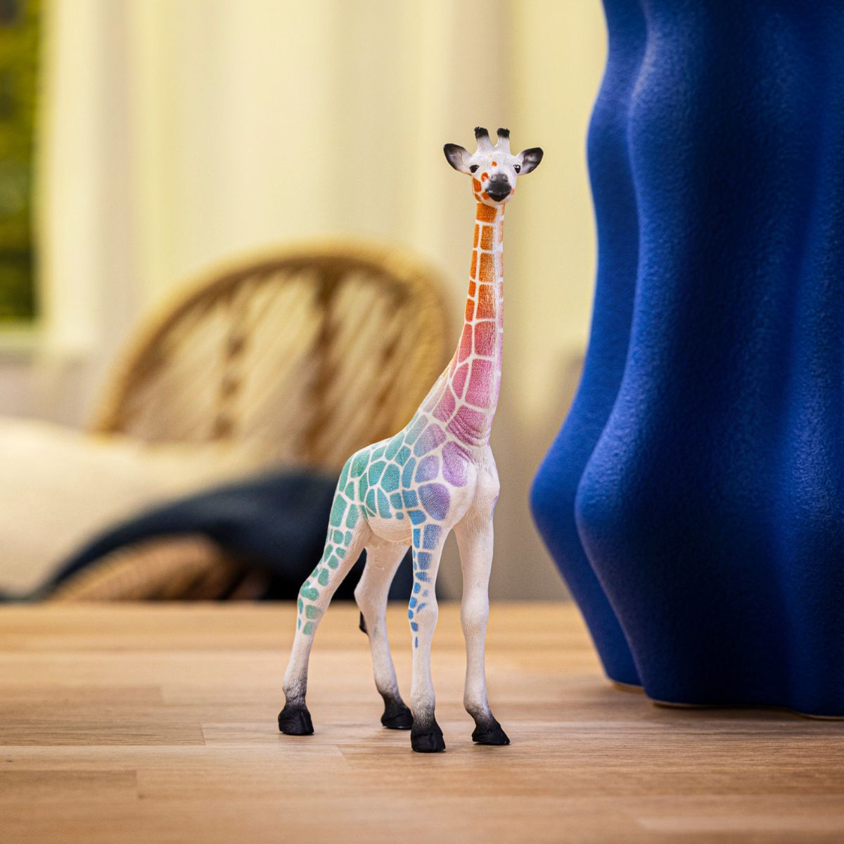 A white toy giraffe with rainbow-colored spots stands on a wooden floor