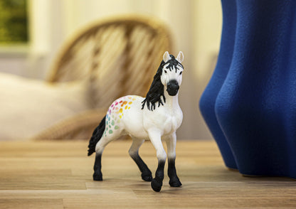 A white horse figurine with black mane and colorful polka dots on its hindquarters stands on a wooden surface