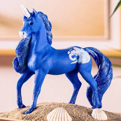 Blue unicorn figurine with white horn, sparkly mane, wave design, standing on sand with seashells