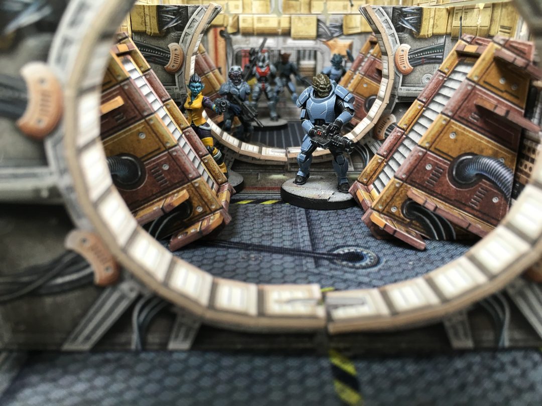 A blue armored sci-fi miniature holding a rifle stands in a detailed futuristic corridor, viewed through a circular bulkhead.