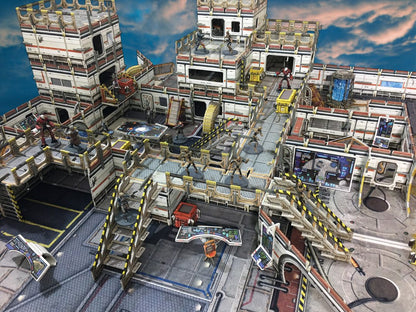 Sci-fi tabletop game: Miniature figures are arrayed across a modular, multi-level futuristic base with stairs and consoles, under a cloudy sky.