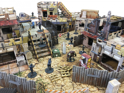 Tabletop game: Armed humanoid and creature miniatures deployed across multi-level, dilapidated buildings and fences in a sci-fi wasteland.