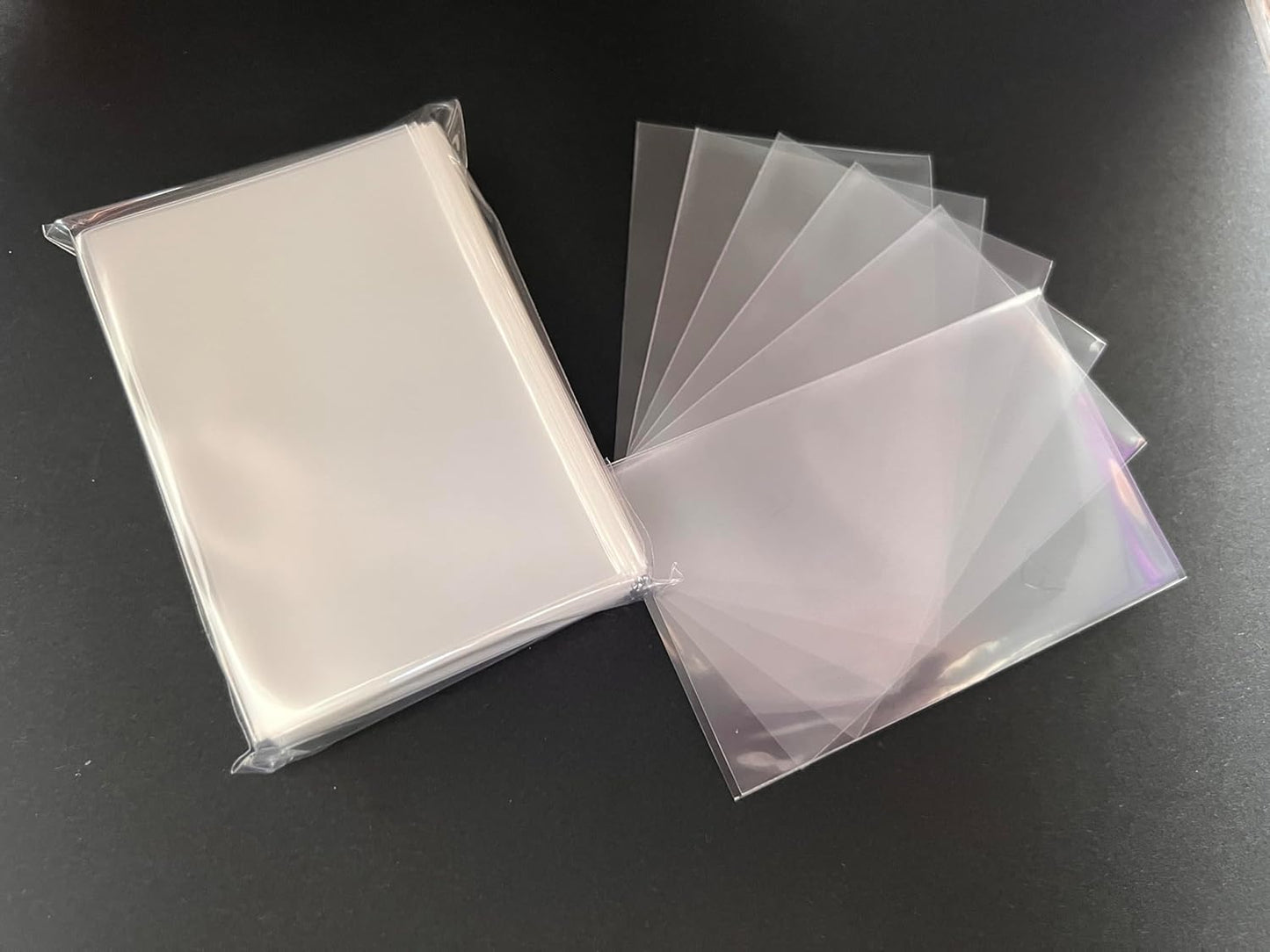 Clear plastic card sleeves: a packaged stack and several fanned out on a dark background