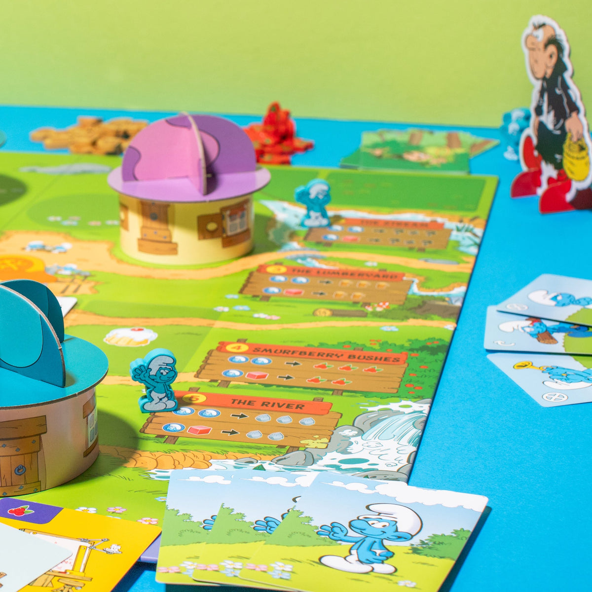 A Smurfs board game is set up, featuring blue Smurf pawns, mushroom houses, character cards, and Gargamel.
