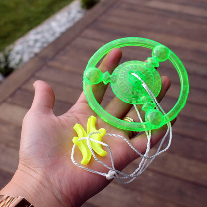Hand holds a bright green string-pulled spinner toy with a yellow banana handle, outdoors