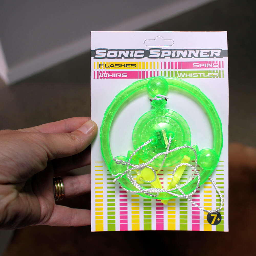 A hand holds a packaged neon green "Sonic Spinner" toy, featuring a round design with a string