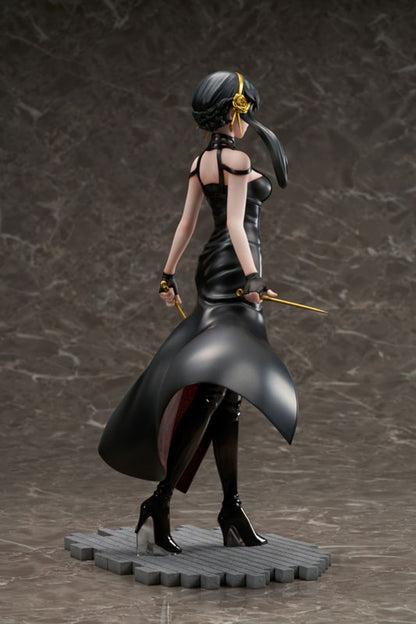 A Spy X Family Yor Forger figure in a black dress and boots, holding two gold weapons, with dark hair and a gold rose accessory, standing on a grey base