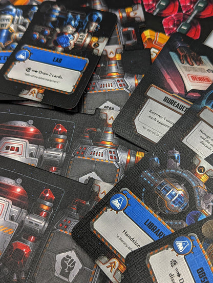 A close-up of scattered sci-fi themed game cards, including "LAB," "BUREAUCRACY," and "LIBRARY," showing futuristic artwork