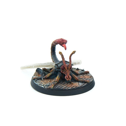 Painted miniature of a dark, insectoid creature with a scorpion tail, raised stinger, and long antennae, on a rocky base