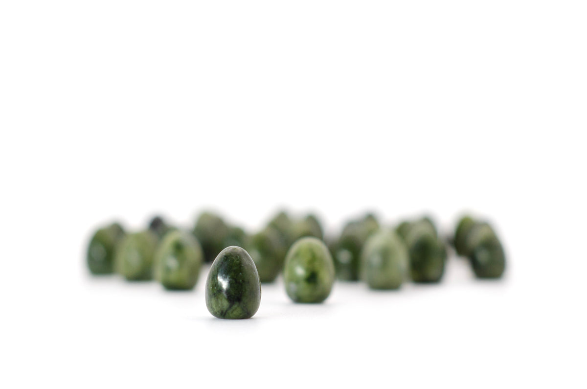 Close-up of a small, polished green mottled stone egg, backed by a blurred row of matching stones on a white background