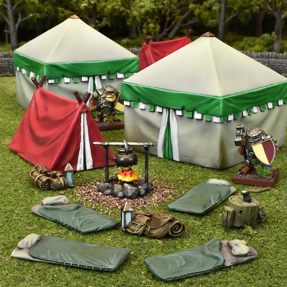 Miniature fantasy camp scene with two large cream &amp; green tents, a red tent, two armored figures, a central campfire with a hanging pot, sleeping bags, and camp gear on grass