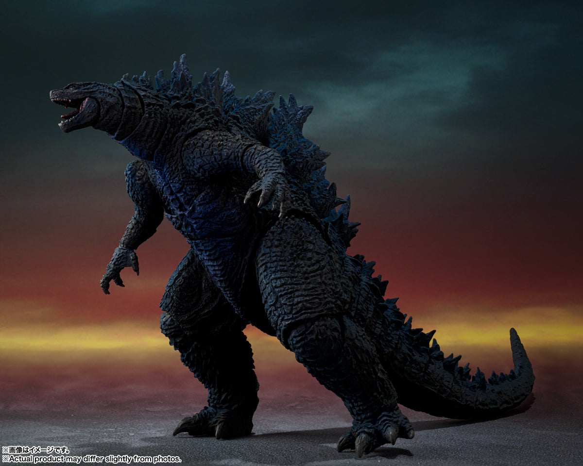 Godzilla figure roars, mouth open, standing against a dark and fiery sky.