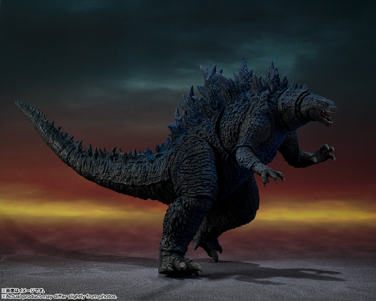 A dark Godzilla figure with prominent spikes, open mouth, and raised claws, stands against a red and blue sky.
