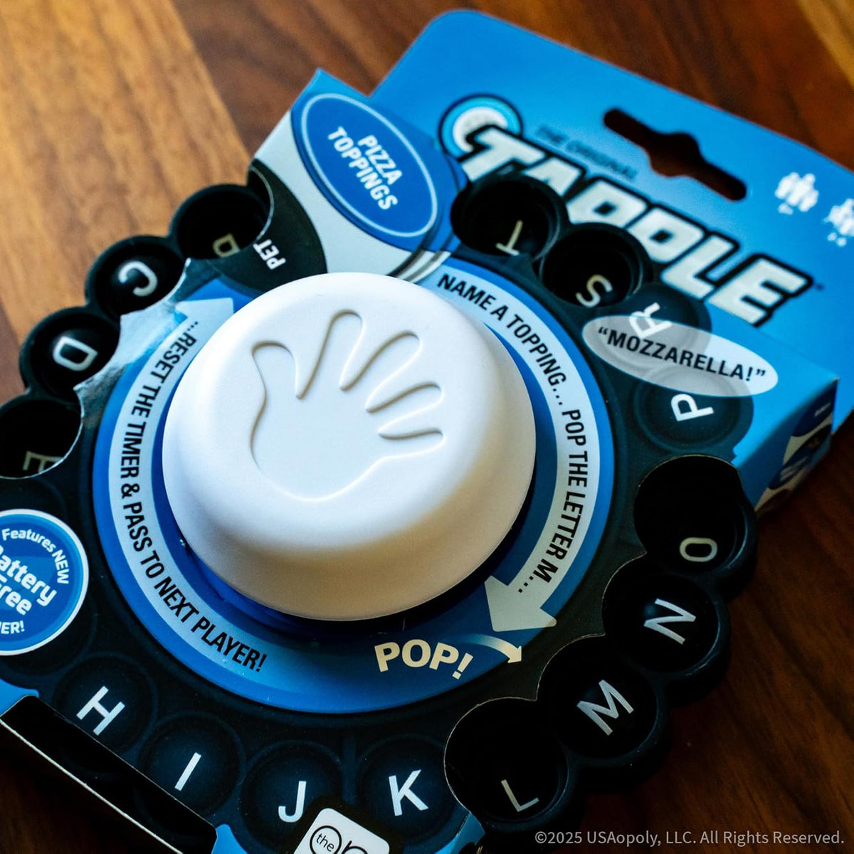 Close-up of the &quot;Gaggle&quot; word game device with a central white handprint button, surrounded by letters and instructions for naming pizza toppings