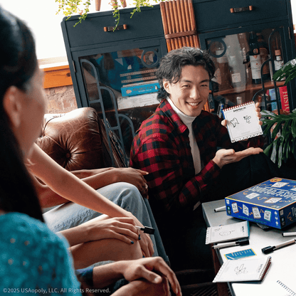 Smiling man in a plaid shirt holds up a sketch, playing Telestrations board game with friends