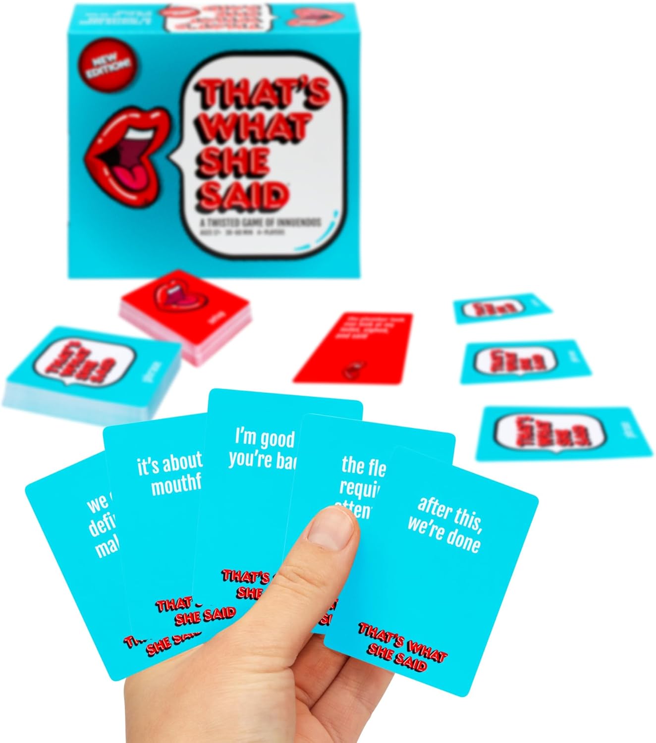 Hand holding blue "That's What She Said" game cards, with the game box and more cards spread on a white surface