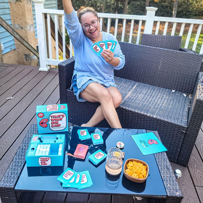 Excited woman on a deck plays "That's What She Said" card game, holding cards and raising an arm