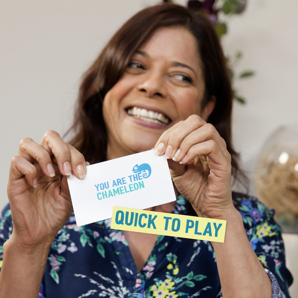 A smiling woman happily displays two game cards: "YOU ARE THE CHAMELEON" and "QUICK TO PLAY"