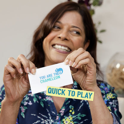 A smiling woman happily displays two game cards: "YOU ARE THE CHAMELEON" and "QUICK TO PLAY"