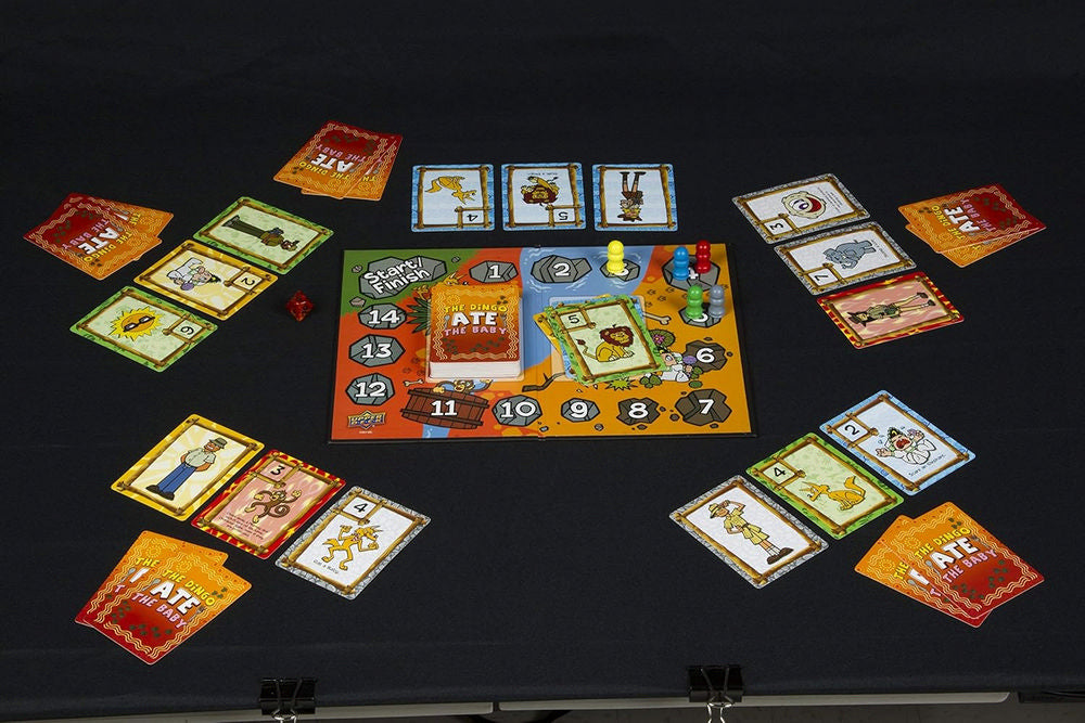 The Dingo Ate The Baby board game laid out on a dark surface, showing the board, cards, pawns, and a die