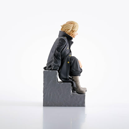 Blonde-haired anime figure in a dark long coat with gold buttons, sitting on gray steps, looking right