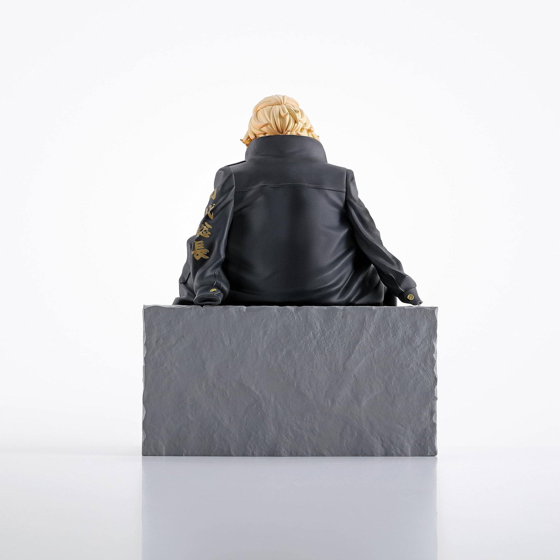 Blonde-haired character figure in a black jacket with gold Kanji, sitting on a gray block, viewed from behind