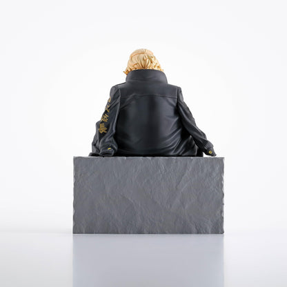 Blonde-haired character figure in a black jacket with gold Kanji, sitting on a gray block, viewed from behind