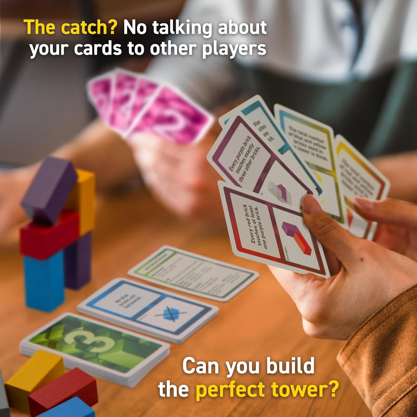 Hands holding game cards for a tower-building board game with colorful blocks on a table