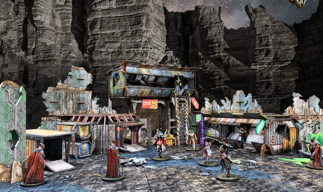 A tabletop wargame scene: armed sci-fi miniatures among modular, ramshackle buildings in a rocky canyon beneath a starry sky.